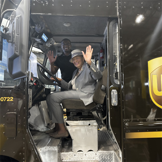 Rep. Adams behind a UPS truck steering wheel with a worker in the truck